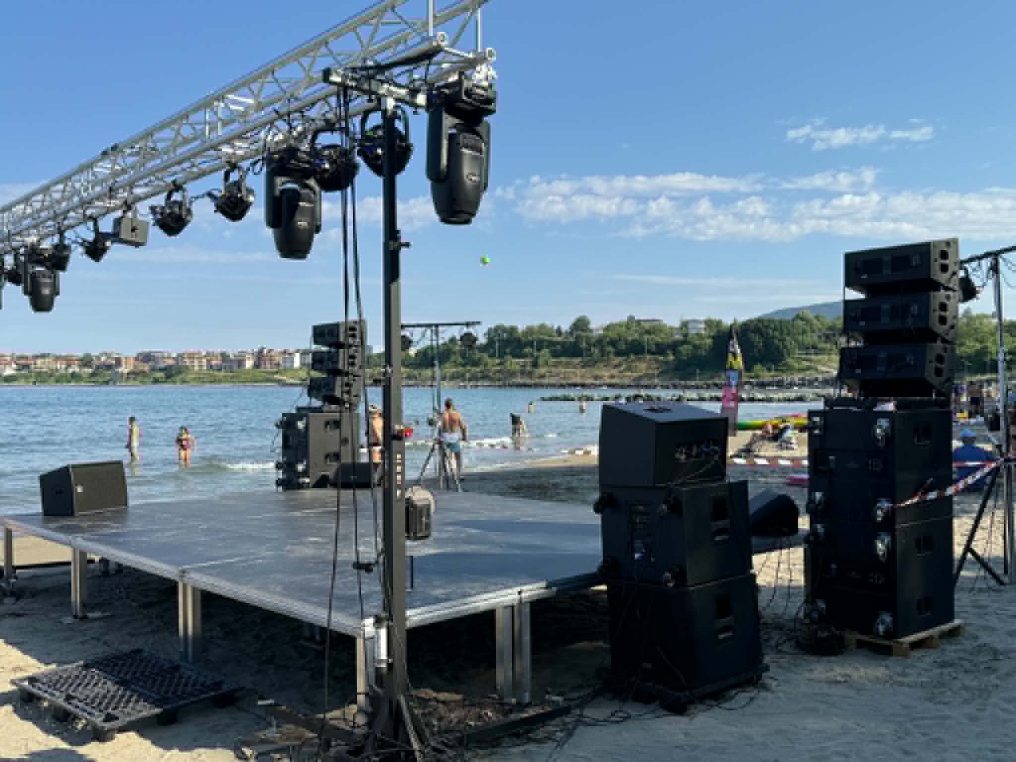 Панорама на плажното парти със сцена, озвучаване и публика край морето